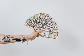 Tattooed arm holding a fan of US dollar bills on a white background, symbolizing wealth and financial success. HD wallpaper