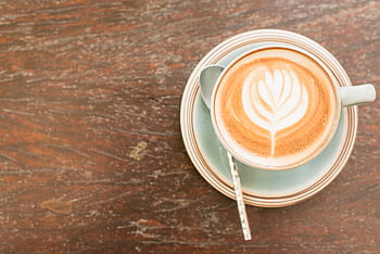 Top view of a coffee cup with latte art on a wooden table, perfect for a cozy morning atmosphere. HD wallpaper
