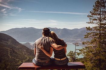 Couple sitting on bench embracing scenic mountain view, embodying romantic nature escape. HD wallpaper