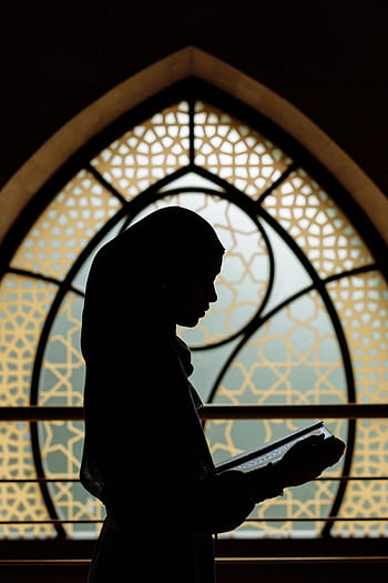Silhouette of a woman reading in front of Islamic-patterned window. Peaceful and cultural ambiance. HD phone wallpaper