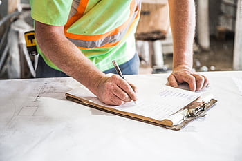 A construction worker writes notes on a clipboard at a construction site, emphasizing planning and precision. HD wallpaper