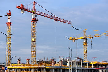 Multiple tower cranes working on a large construction site with blue sky backdrop. HD wallpaper