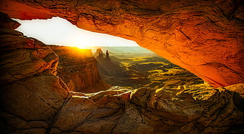Captivating view of sunrise through Mesa Arch, showcasing breathtaking rock formations and desert landscape. HD wallpaper