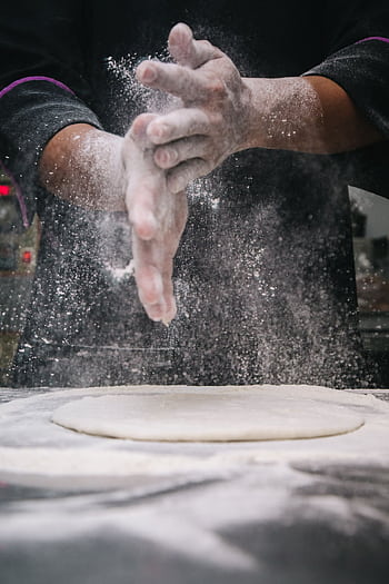 A chef clapping hands over dough, releasing flour in a kitchen setting. HD phone wallpaper