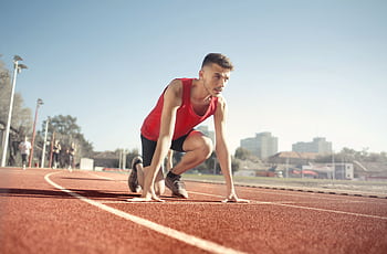 Young male athlete in start position on outdoor track, ready to sprint. HD wallpaper
