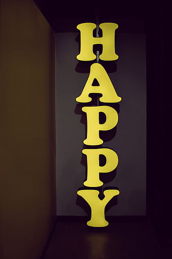 Illuminated yellow 'HAPPY' sign displayed vertically in a dimly lit hallway setting, evoking a playful mood. HD phone wallpaper