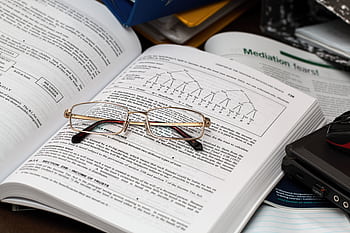 An open book with reading glasses, surrounded by study materials and a laptop, ideal for education themes. HD wallpaper