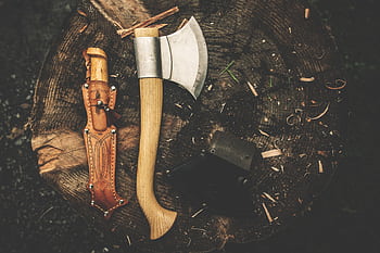 A rugged camping axe and knife on a tree stump, perfect for bushcraft and outdoor adventures. HD wallpaper