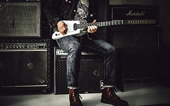A musician plays an electric guitar in a studio, surrounded by amplifiers, showcasing rock and punk vibes. HD wallpaper