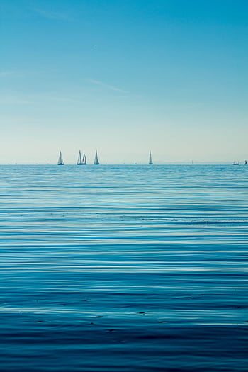 Calm ocean view with sailboats on the horizon under a clear blue sky. HD phone wallpaper