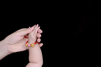 Close-up of a mother gently holding her baby's hand with a red bracelet, symbolizing love and care. HD wallpaper
