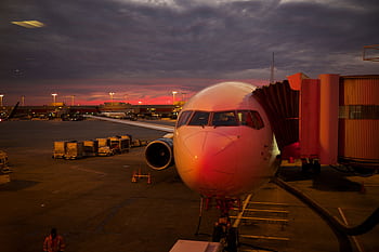 Plane boarding at sunset with vibrant sky colors and airport lights. HD wallpaper