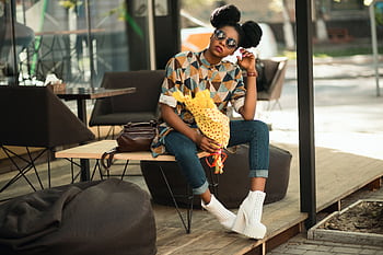 Trendy woman with sunglasses and flowers relaxing on a patio bench in sunlight. HD wallpaper