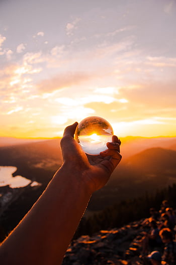 Captivating sunset view reflected in a crystal ball held by hand, overlooking a scenic landscape. HD phone wallpaper