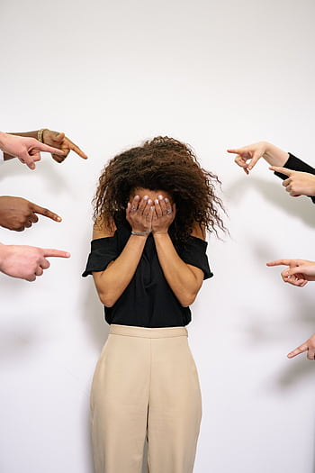 A stressed woman covers her face as multiple hands point accusatorily in a studio setting. HD phone wallpaper