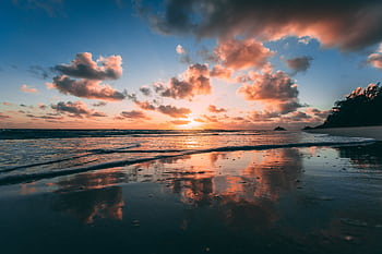 A beautiful sunrise over Kailua Beach with vibrant clouds reflected in the calm ocean water. HD wallpaper