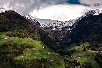 Scenic view of an alpine valley with lush greenery and snow-capped mountains under a cloudy sky. HD wallpaper