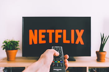 A hand holding a TV remote in front of a screen with Netflix, perfect for streaming and movie night themes. HD wallpaper