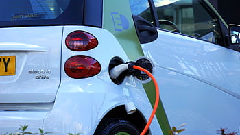 Close-up of an electric car being charged, highlighting eco-friendly transportation. HD wallpaper