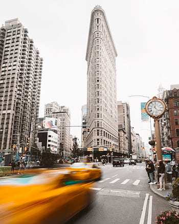 Iconic Flatiron Building with busy street and blurred yellow taxi capturing the essence of New York City. HD phone wallpaper