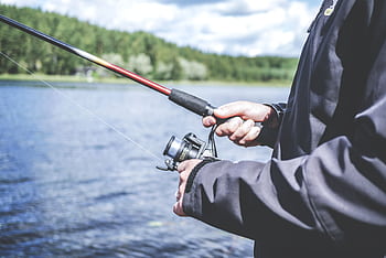 A man enjoys fishing at a lake, showcasing a relaxed outdoor hobby in nature. HD wallpaper