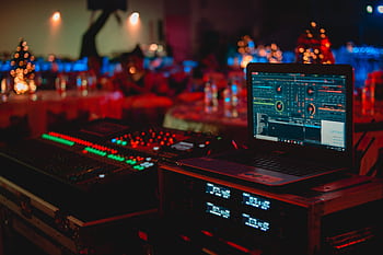 Vivid DJ setup with laptop and sound mixer at a lively indoor event. HD wallpaper