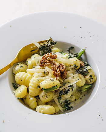 Elegant plate of gnocchi pasta topped with kale and walnuts, perfect for a gourmet meal. HD phone wallpaper