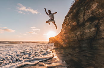 A man jumps off a cliff at sunset in Encinitas, California, capturing a moment of adventure by the sea. HD wallpaper