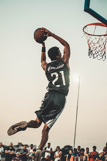 A dynamic basketball player executing a slam dunk during a vibrant outdoor game. HD phone wallpaper