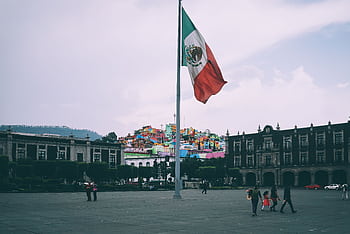 Colorful cityscape of Toluca with large Mexican flag in the foreground, vibrant buildings in the backdrop. HD wallpaper