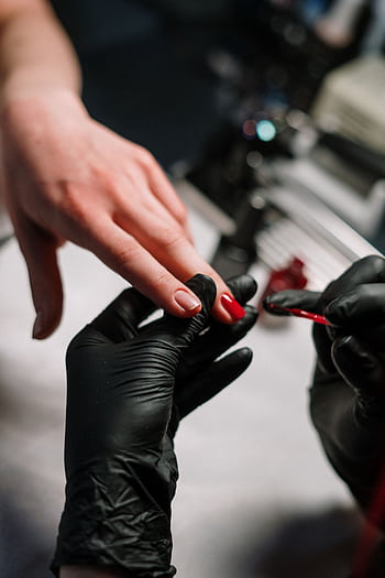 Close-up of a nail artist applying polish with precision using black gloves in a salon setting. HD phone wallpaper