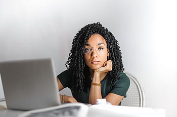 Young woman with glasses working attentively on a laptop at a bright desk. HD wallpaper