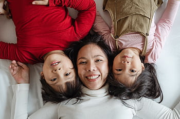 Joyous mother with her children lying on bed, capturing a happy moment of togetherness. HD wallpaper