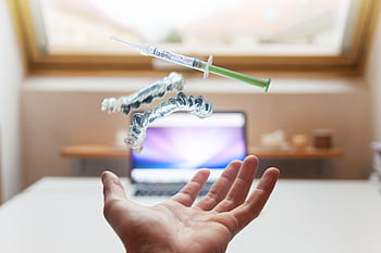 A syringe and dental aligner float above a hand in a modern office, signifying advanced dental care technology. HD wallpaper