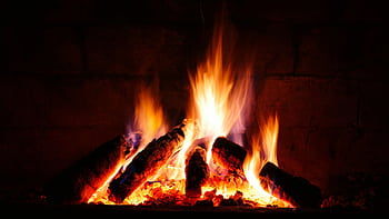 A close-up view of a crackling fire with glowing logs in a cozy fireplace. HD wallpaper