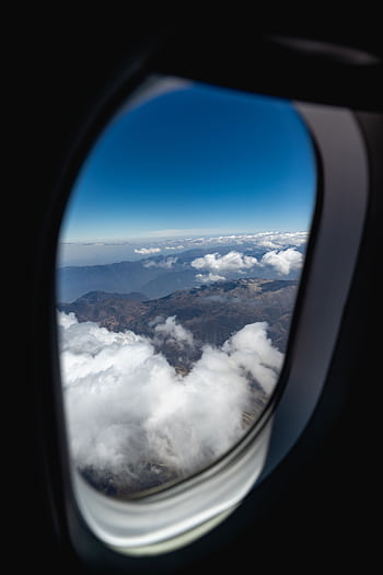 A breathtaking aerial view of clouds and mountains through an airplane window. HD phone wallpaper