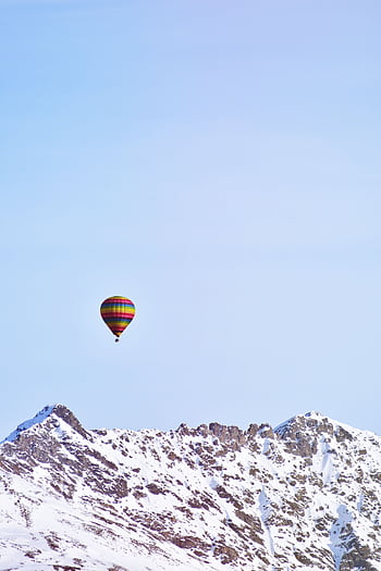 A colorful hot air balloon drifts over majestic snowcapped mountains under a clear blue sky. HD phone wallpaper