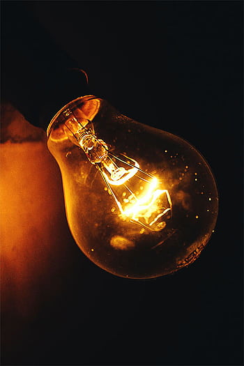 Close-up of a glowing incandescent light bulb illuminating a dark space. HD phone wallpaper