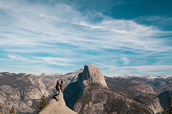 A woman and child stand atop Half Dome, Yosemite, with breathtaking views of the mountain range. HD wallpaper