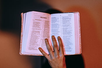 A close-up of a hand holding an open Bible, displaying Proverbs under warm lighting. HD wallpaper
