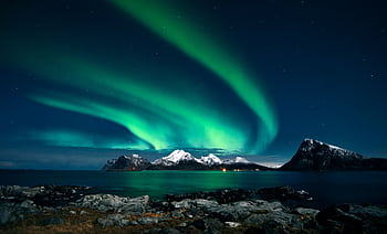 Breathtaking northern lights display over snow-covered mountains and serene waters in Lofoten, Norway. HD wallpaper
