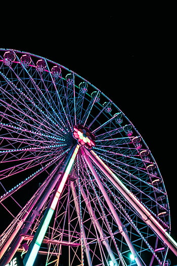 A brightly illuminated Ferris wheel with vibrant lights stands tall against the night sky in a theme park. HD phone wallpaper