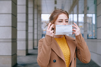 Young woman adjusting her face mask in an urban outdoor setting, promoting health safety and prevention. HD wallpaper