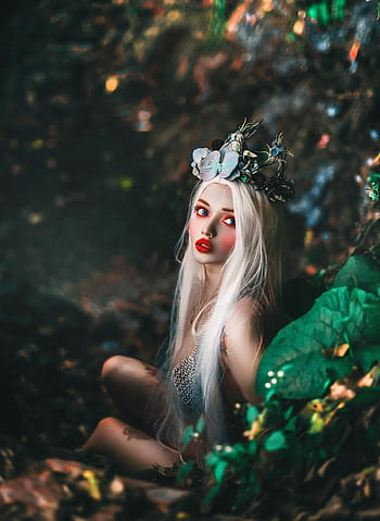 A blonde fairy with a floral crown sits amidst an enchanted forest, exuding fantasy and glamour. HD phone wallpaper