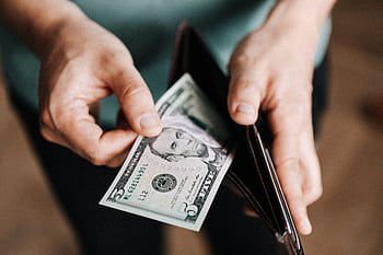 A person taking a five dollar bill from a wallet symbolizing personal finance and budget management. HD wallpaper