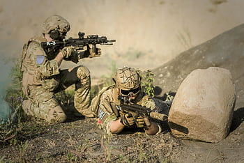 Two soldiers in camouflage uniforms practice tactical maneuvers in a desert environment, exhibiting teamwork and precision. HD wallpaper