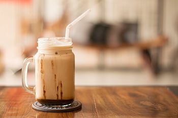 Close-up of iced coffee in a mason jar on a wooden table, perfect for a café vibe. HD wallpaper