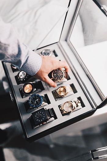 A sophisticated display of luxury watches in an elegant case with a hand selecting one. HD phone wallpaper