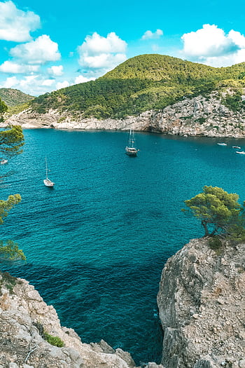 Sailboats drift in a stunning turquoise bay surrounded by rocky cliffs in Ibiza, Spain. HD phone wallpaper