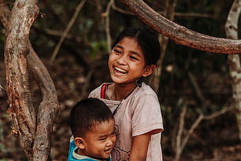 Happy siblings laughing together while playing outside among trees. HD wallpaper